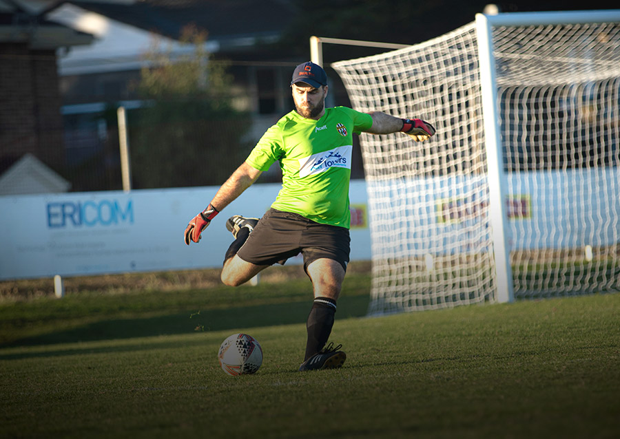 Man in a green shirt kicking a ball in a football field